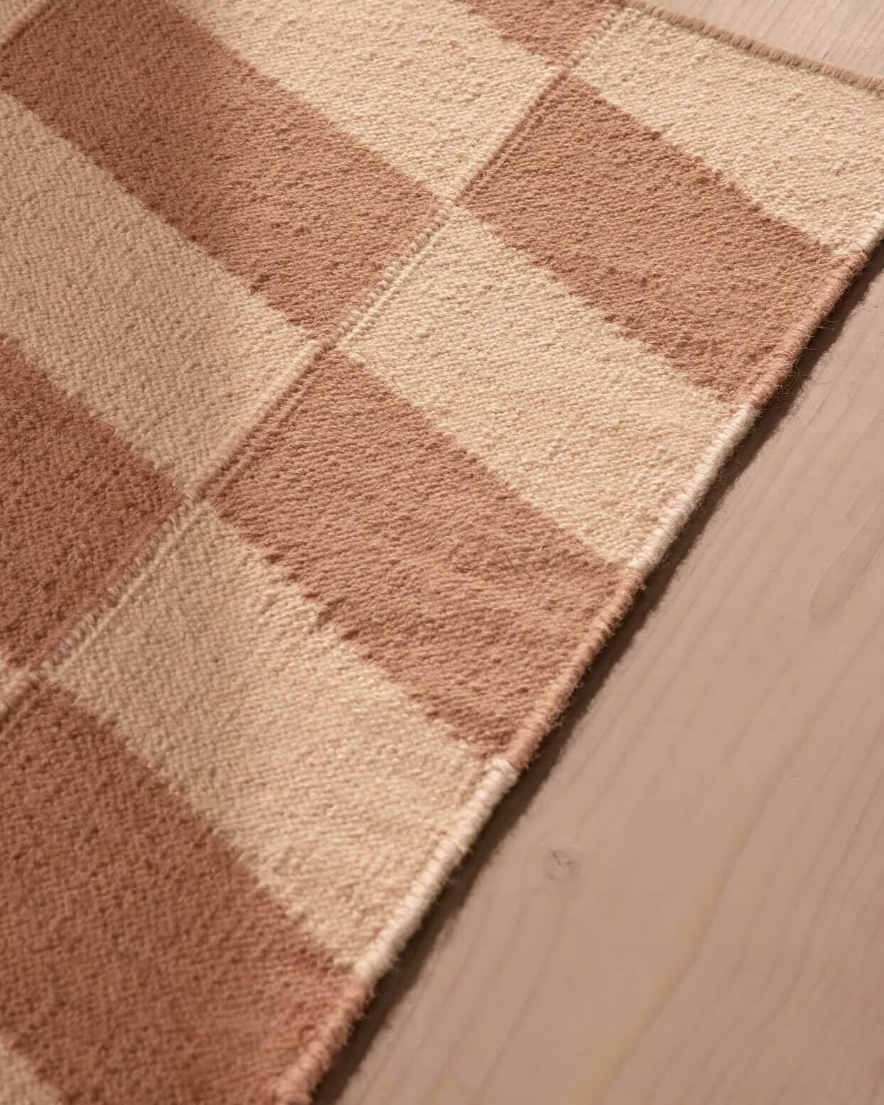 close-up of checkered rug with brown and beige squares on a wooden floor