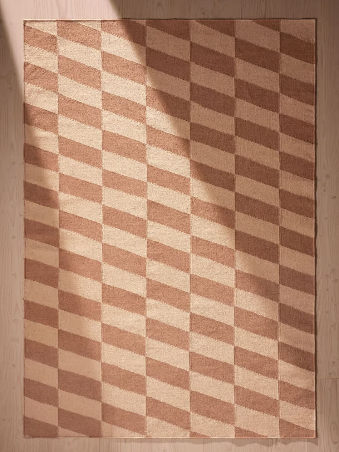 Checkered patterned handwoven rug with brown and beige colors on a wooden floor.