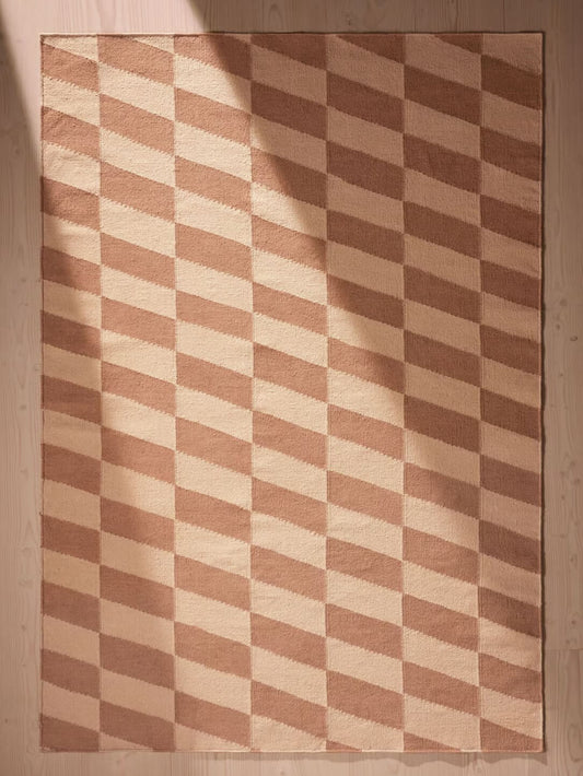 Checkered patterned handwoven rug with brown and beige colors on a wooden floor.