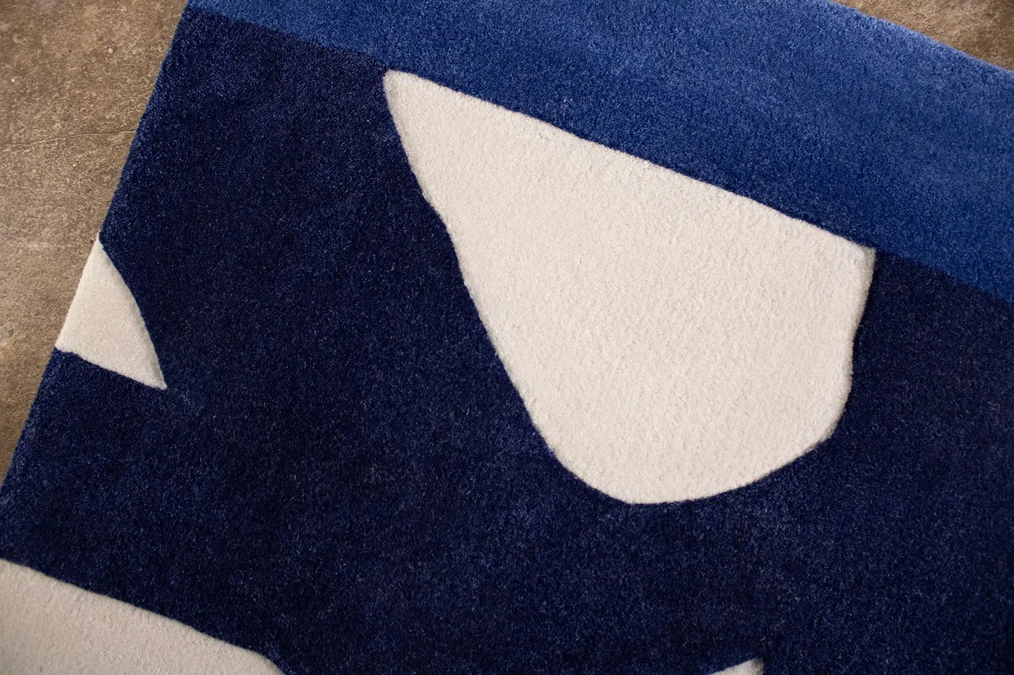 Close view of navy blue and beige abstract patterned rug on a brown floor.