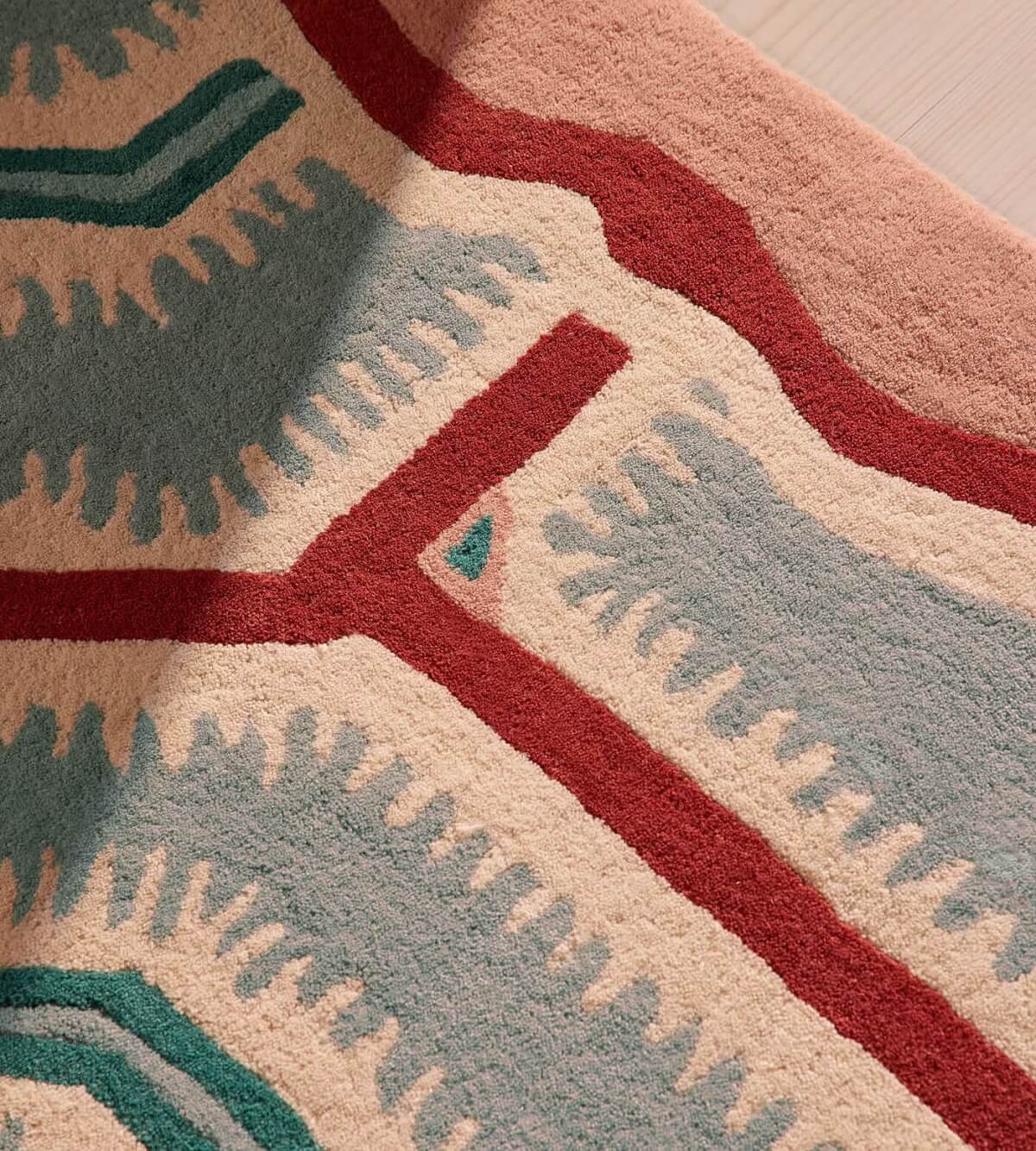 Close-up of a hand tufted patterned rug with red, green, and beige colors.