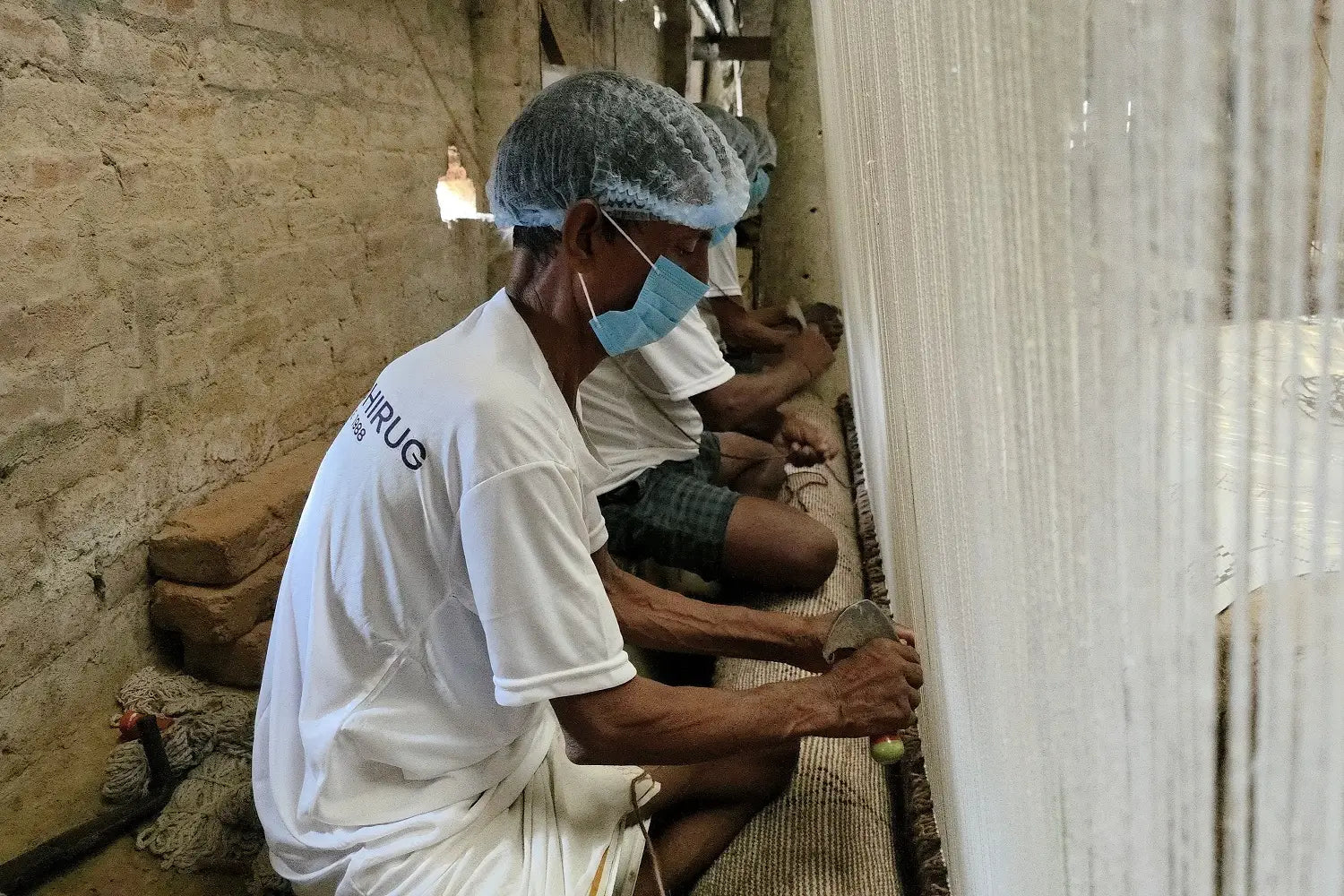 Person making a hand knotted rug on a loom in a workshop setting
