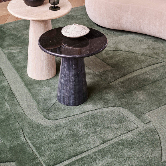 Modern black side table on a hand tufted abstract green wool and silk rug with geometric patterns