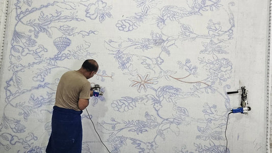 A rug artisan is tufting onto a design printed stretched canvas.