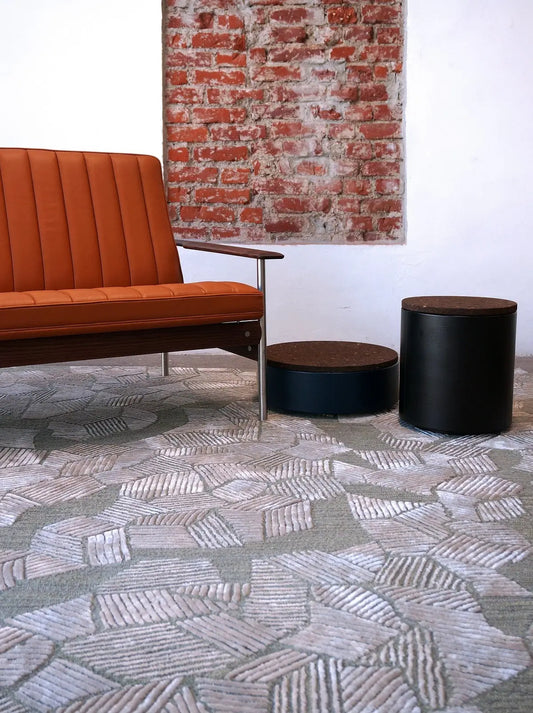 a room with a geometric design patterned wool and silk carpet, sofa, black cylindrical stools