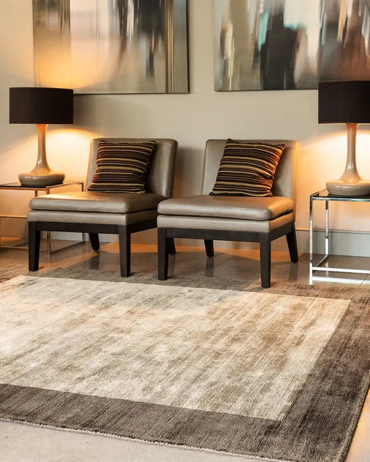 mocha border hand woven viscose rug in a living room with two gray chairs.