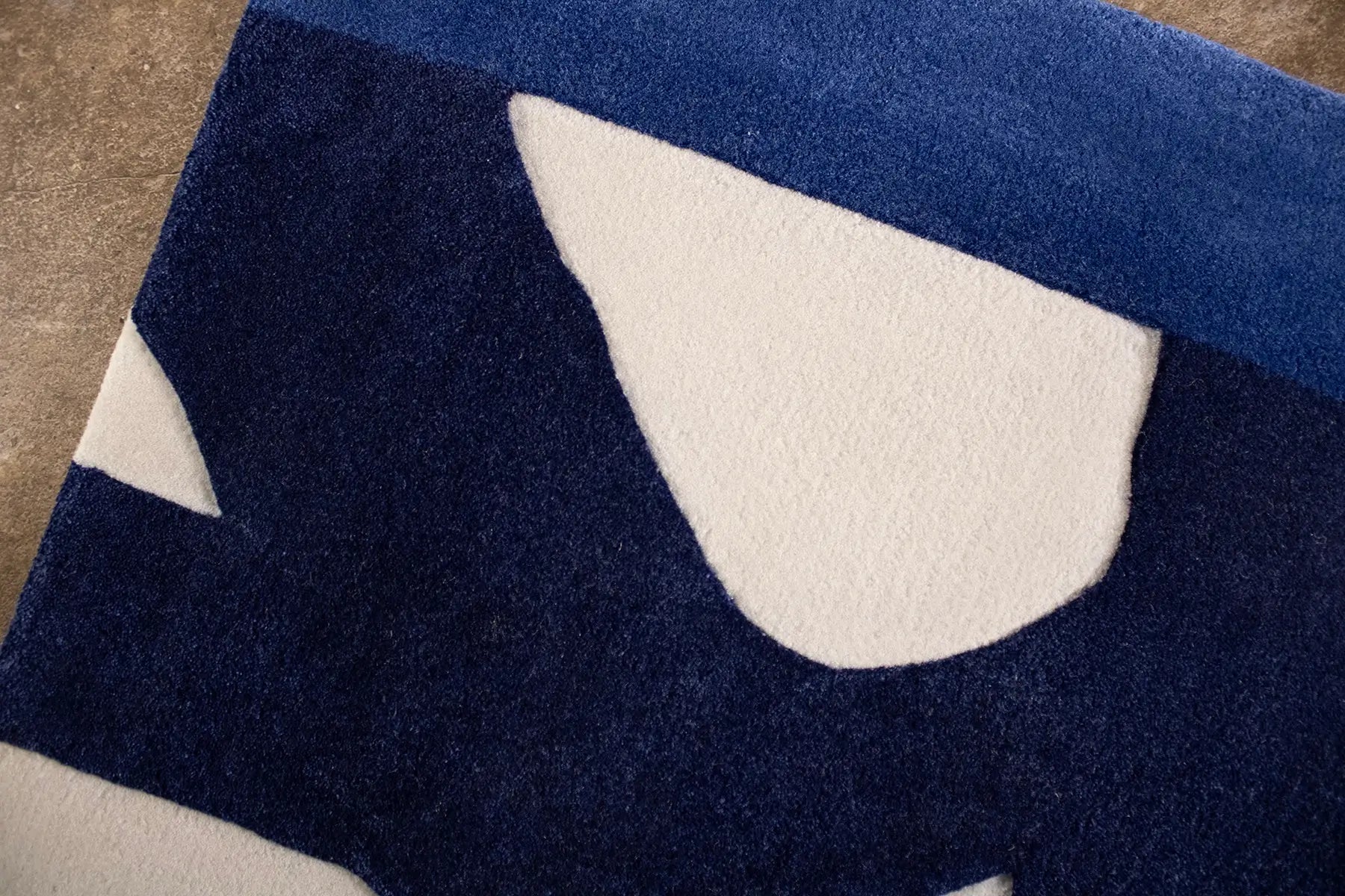 Close view of navy blue and beige abstract patterned rug on a brown floor.