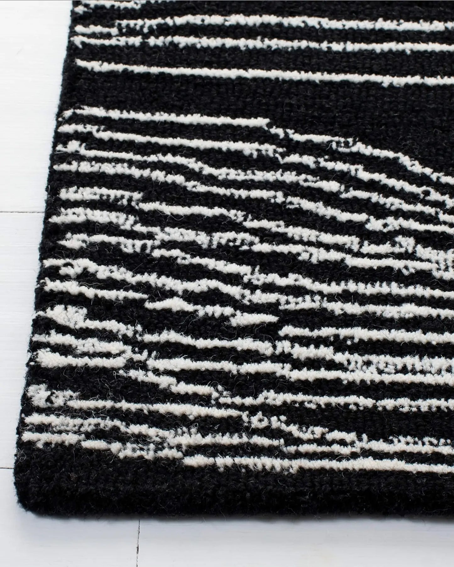 Close-up of a black and white wave line rug on a white floor.