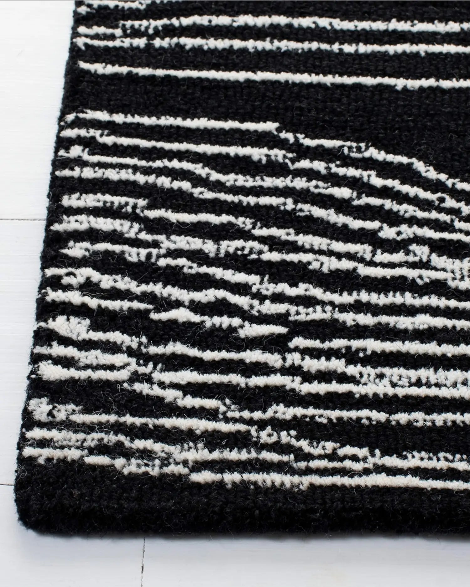 Close-up of a black and white wave line rug on a white floor.