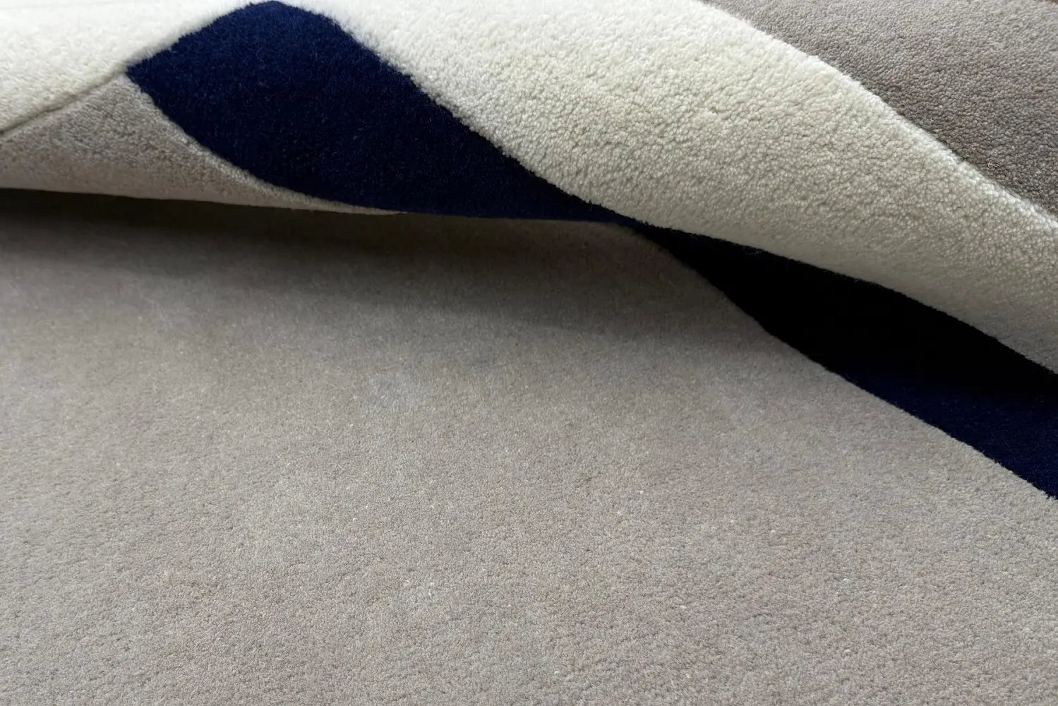 Close-up of gray hand tufted wool rug with a white border and a blue accent line