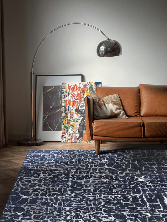 Living room with modern hand tufted blue and white pattern rug, a brown sofa and floor lamp.