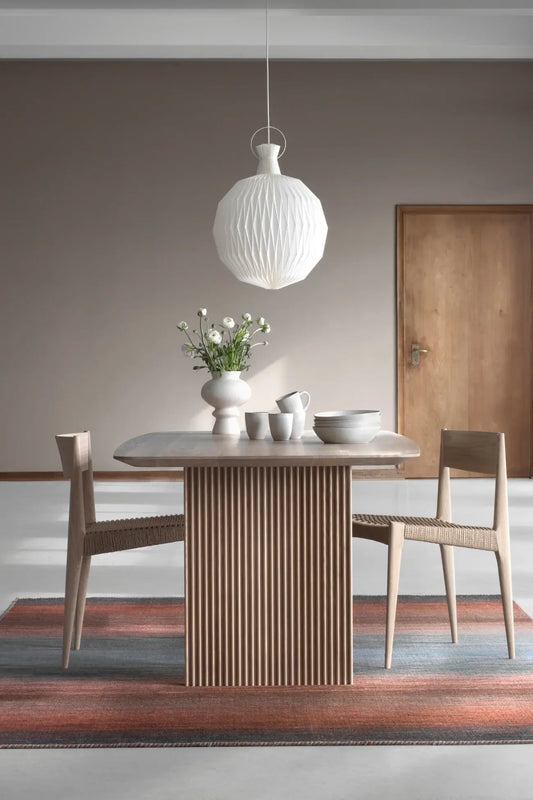 hand woven wool rug in dining room with a wooden table and chairs, white pendant light, and decorative elements.