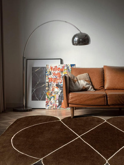 modern brown wool rug and leather sofa in a living room with a floor lamp and artwork on the wall.
