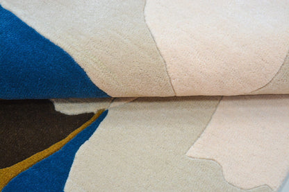 Close-up of a hand tufted wool rug with abstract patterns in blue, beige, and brown.