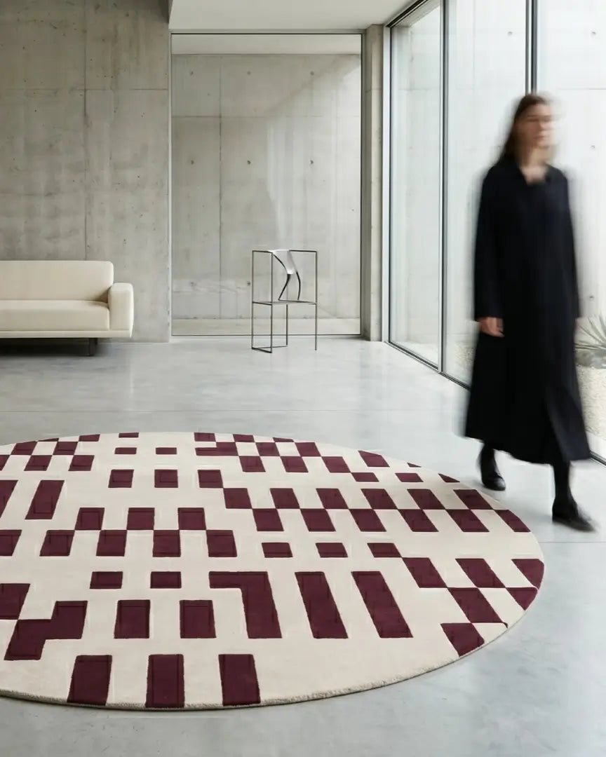 Round rug with a red and beige geometric pattern on floor.