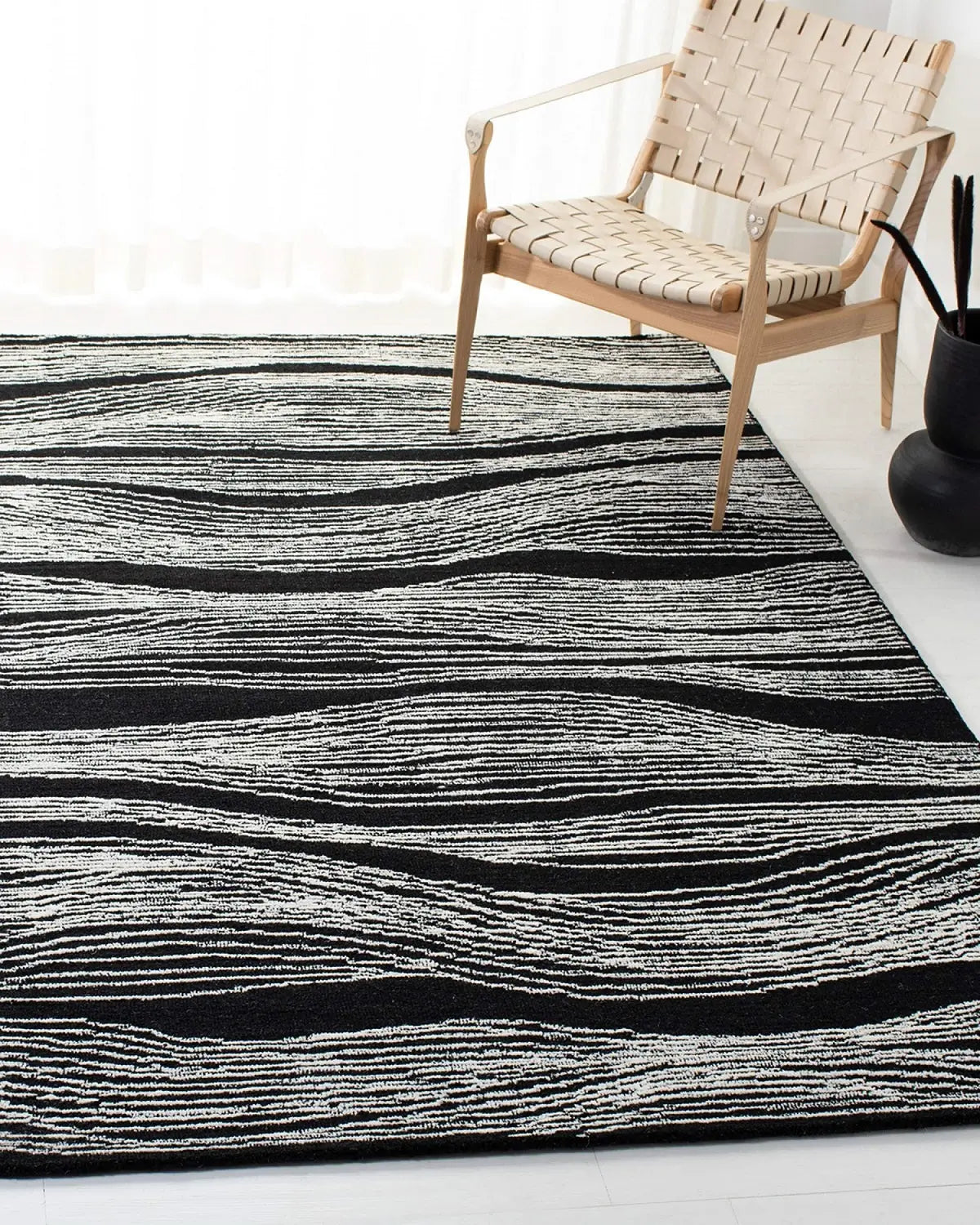 Hand tufted black wool rug with white wave design and a wooden chair on it.