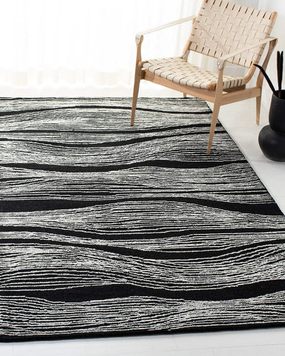 Hand tufted black wool rug with white wave design and a wooden chair on it.