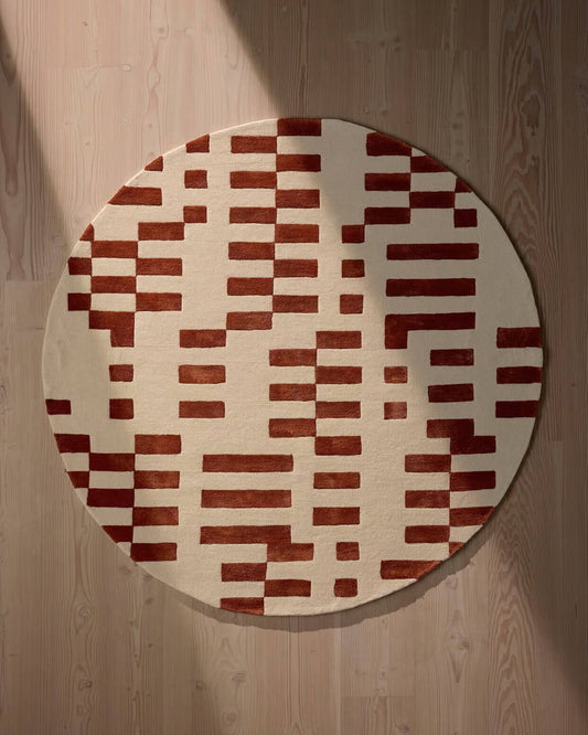 Round rug with a red and beige geometric pattern on a wooden floor.