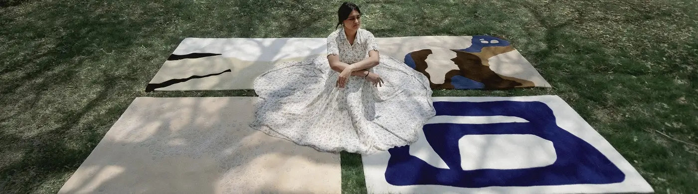 Woman in a white dress sitting on  abstract rugs outdoors.